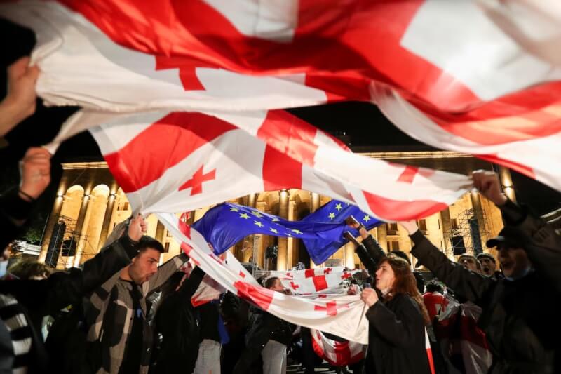 示威者13日舉起喬治亞國旗與歐盟旗幟抗議境外影響力法案。（路透社）