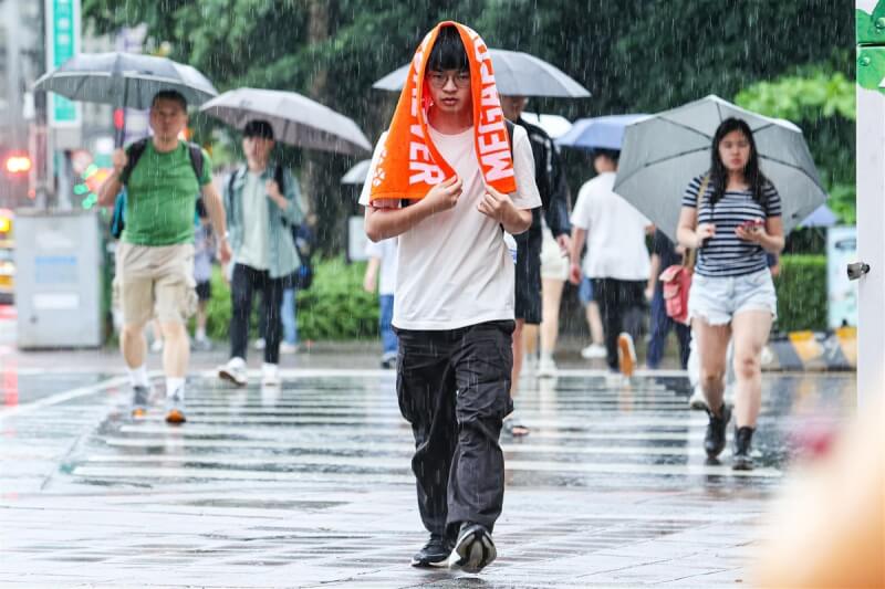 台北市午後降下陣雨，有行人披著毛巾穿越馬路。（中央社檔案照片）