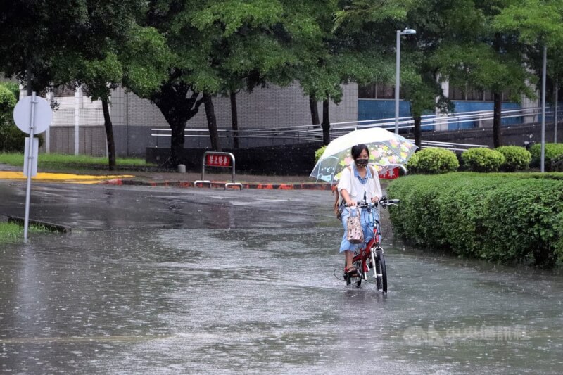 新莊民眾撐著傘騎腳踏車經過積水的道路。（中央社檔案照片）
