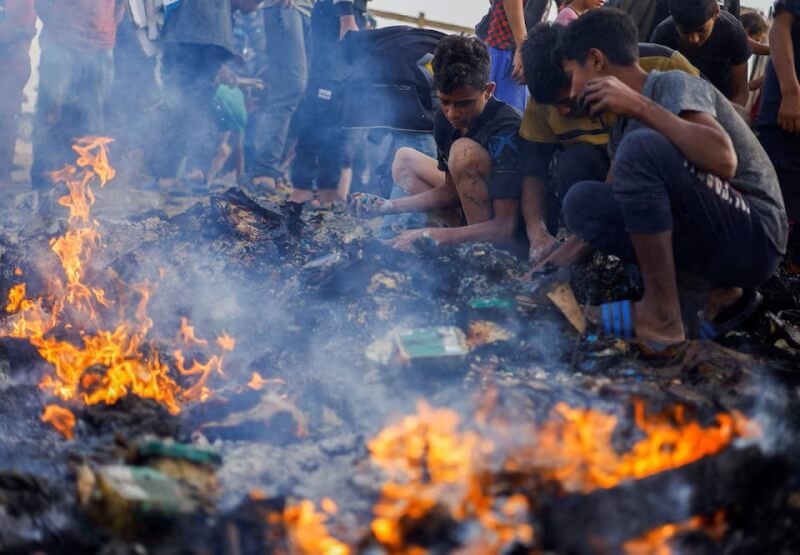 巴勒斯坦難民27日在遭以色列空襲炸毀的營地餘燼旁尋找食物。（路透社）