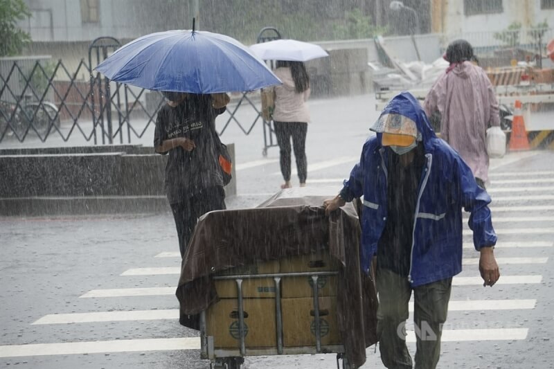 圖為高雄市三民區民眾撐傘、穿雨衣快步過馬路。（中央社檔案照片）