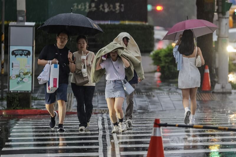 圖為台北市信義區行人以外套遮擋雨勢，快步過馬路。（中央社檔案照片）
