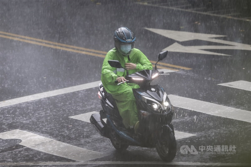 機車騎士行經台北市松山區遇上大雨，拉緊雨衣避免進水。（中央社檔案照片）