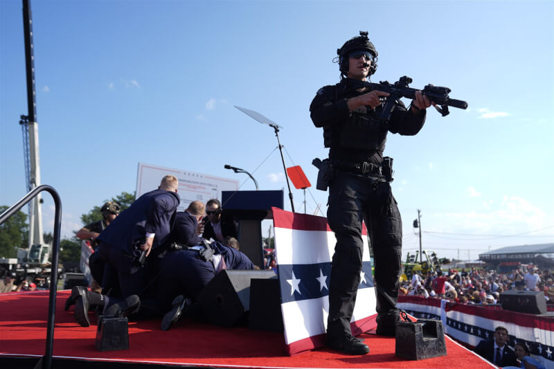 美國前總統川普13日在賓州造勢大會遇襲，特勤局人員立即到講台旁掩護川普。（美聯社）