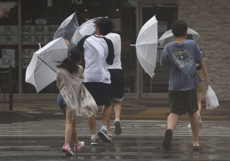 圖為28日鹿兒島市出現強烈風雨，民眾撐傘走在路上。（共同社）