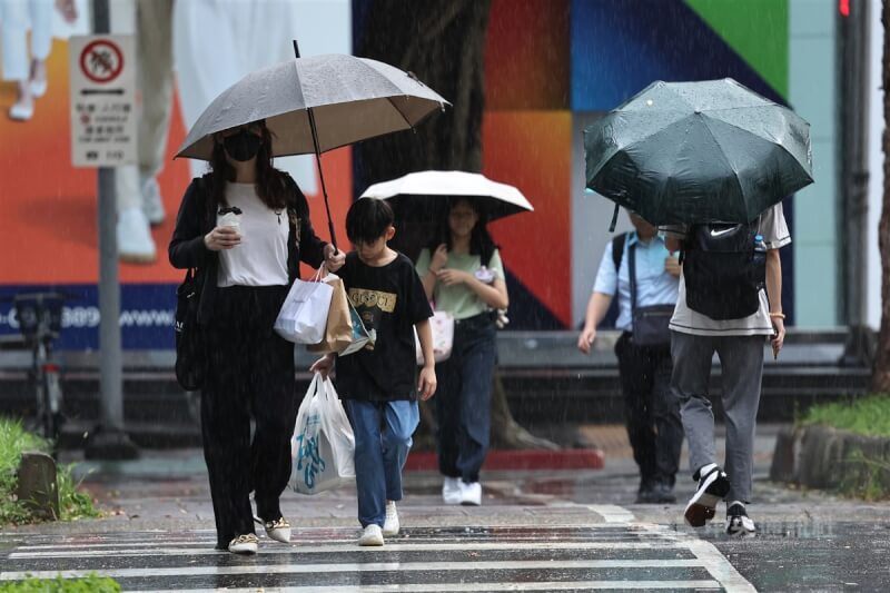 松山區街頭民眾撐起傘走過馬路。（中央社檔案照片）