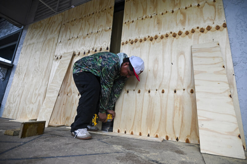 颶風密爾頓登陸前，佛州一名工人8日用木板封住玻璃。（法新社）