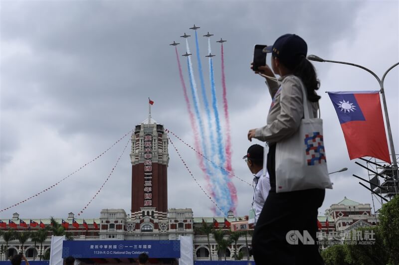 空軍雷虎小組7架AT3教練機編成五角隊形，施放紅藍白3色彩煙低空通過總統府上方，民眾拿起手機記錄精彩一刻。中央社記者趙世勳攝 113年10月10日