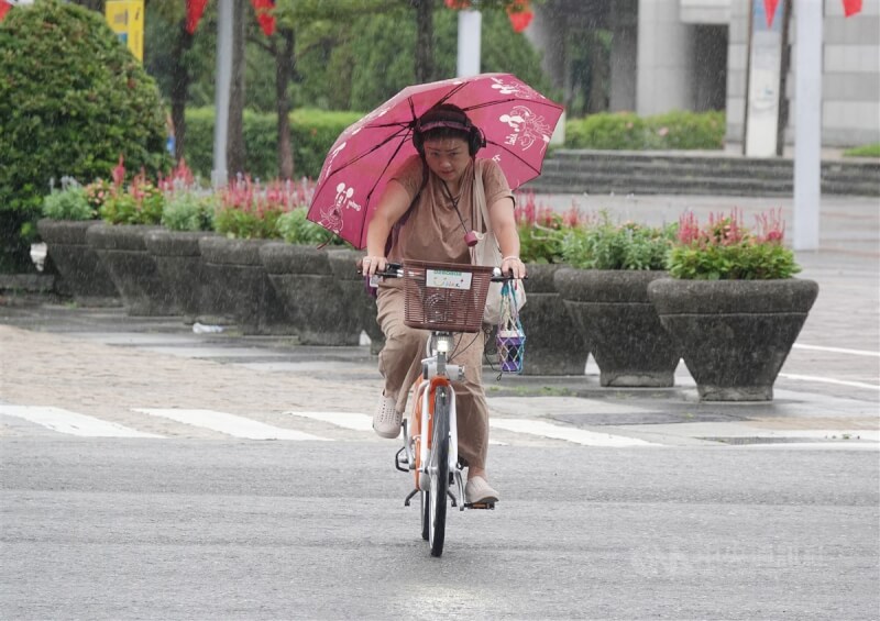 圖為台北市信義區局部大雨，民眾騎自行車用頭夾著傘遮擋雨勢。（中央社檔案照片）