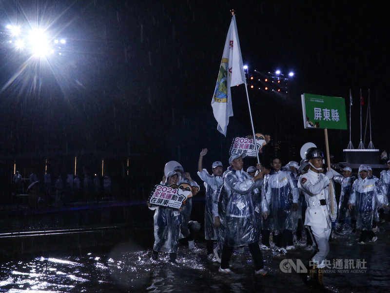 全民運動會26日在大雨中開幕，場地屏東縣民公園多處積水，選手踏水進場，表演者也在雨中登台。中央社記者黃郁菁攝  113年10月27日