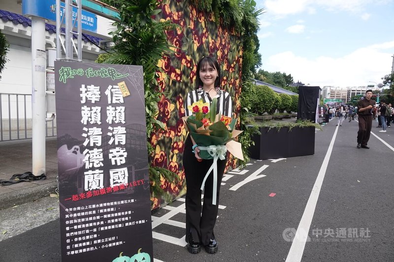 民眾黨27日在台北市愛國東路封街舉辦萬聖節活動「賴政府,搞什麼鬼?」,發言人吳怡萱拿著蘭花在「賴清德蘭」網美花牆前拍照。中央社記者鄭傑文攝 113年10月27日