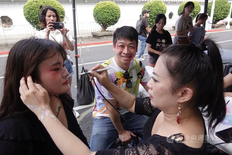 民眾黨27日在台北市愛國東路封街舉辦萬聖節活動「賴政府,搞什麼鬼?」,專業彩妝師在現場設置彩繪區,協助副秘書長許甫(中)、民眾進行特效化妝。中央社記者鄭傑文攝 113年10月27日