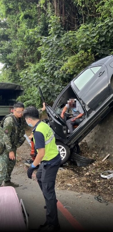 新竹縣新豐鄉松柏林路27日下午發生車禍，1輛自小客車擦撞在路旁軍方交管人員後撞向邊坡，整輛車卡在邊坡上，造成2人受傷送醫。（新竹縣政府消防局提供）中央社記者魯鋼駿傳真  123年10月27日