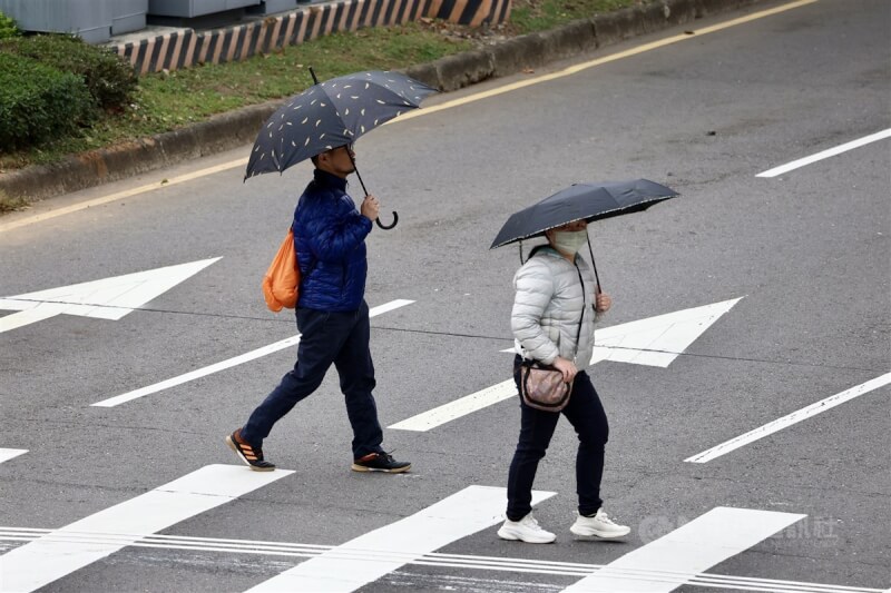 圖為台北市士林區民眾穿上羽絨外套、撐傘過馬路。（中央社檔案照片）