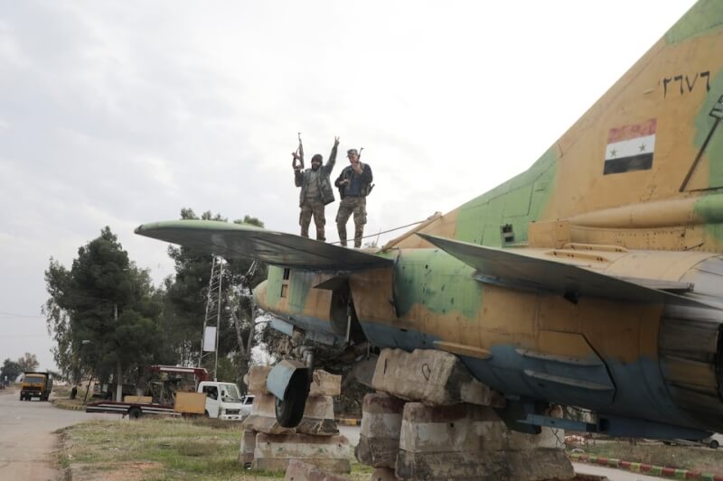 敘利亞反抗軍7日站在位於哈瑪的政府軍用飛機上比出勝利手勢。（路透社）