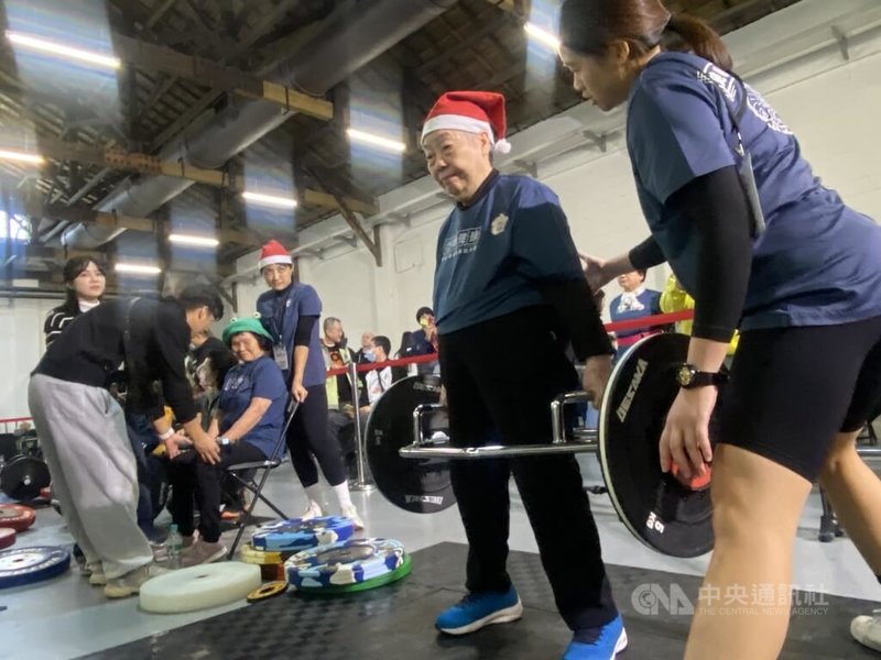 90歲阿嬤鄭陳金梅(右2)原本因車禍,走路都得拿拐杖,後來在家人鼓勵下開始運動、找回身體主控權,21日開心參加「聖誕老人硬舉大賽」並順利完賽。圖為鄭陳金梅上場前先在後台熱身。中央社記者吳欣紜攝 113年12月21日