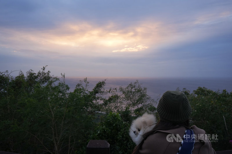 位在恆春半島西南方的關山別名「高山巖」，每年歲末總有遊客來追最後一道夕陽，31日有一組「毛孩旅行團」更專程從台北前來搶看2024年最後日落，李姓團員抱著愛犬一同欣賞夕陽。中央社記者黃郁菁攝 113年12月31日