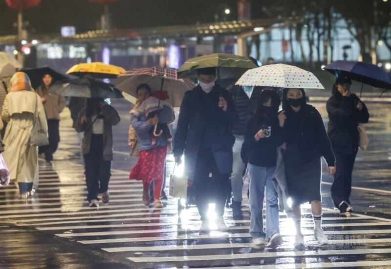 台北市松山區飄雨，外出民眾穿著厚外套撐傘避雨。（中央社檔案照片）