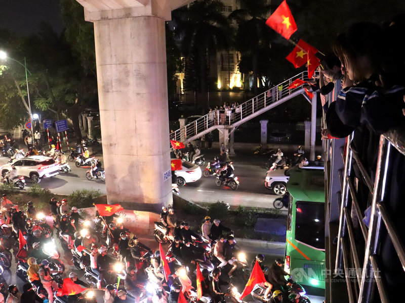 越南5日晚間扳倒泰國成為2024年東協足球錦標賽冠軍,民眾手持越南國旗站在天橋上望著在馬路上「滴胞」(di bao)慶祝的摩托車大軍並一邊大喊「越南無敵」。中央社記者陳家倫河內攝 114年1月6日
