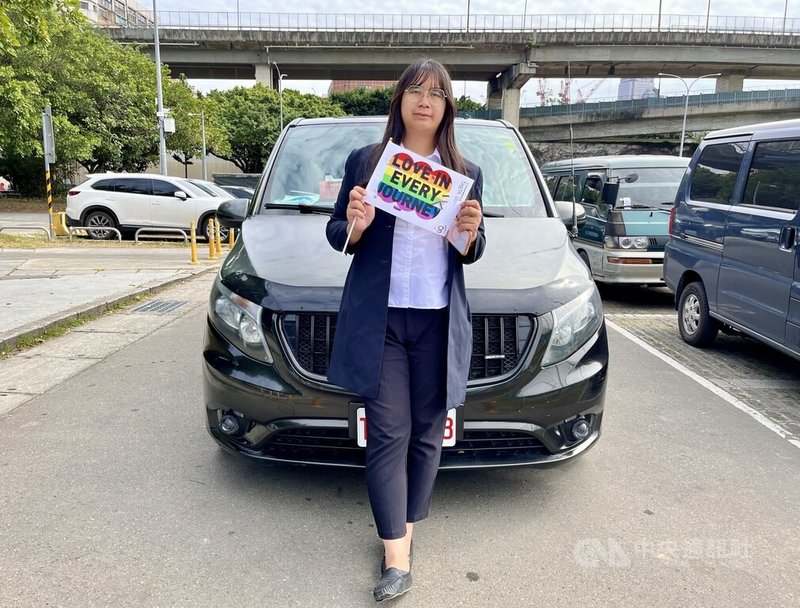 手持寫有「愛在每段旅程」字樣的彩虹旗,邱芯妤站在自己的車前,回顧那條尚未完成、尋求社會與家人更接納跨性別者的艱辛之路。圖攝於114年1月18日。中央社記者黎桑尼攝 114年1月27日