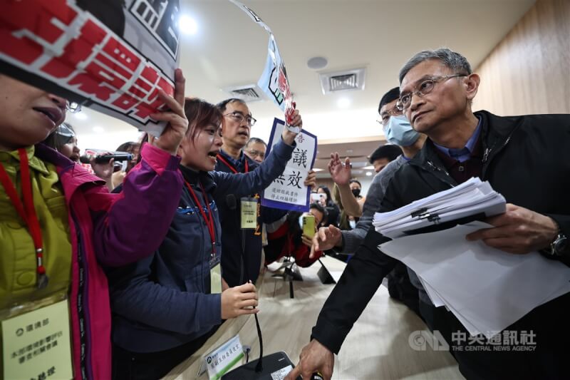 環境部環評大會26日審查四接案,上午因爆發衝突休息至中午12點,中午開會時間到,正反方民眾便再次相互叫囂,並在主席台前舉標語抗議。圖右為環境部政務次長葉俊宏。中央社記者翁睿坤攝 114年2月26日