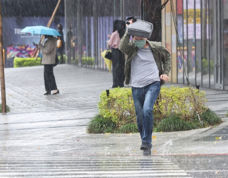 圖為台北市降下大雨,街頭未帶雨具民眾只能先以隨身物品遮擋,快跑過馬路。(中央社檔案照片)