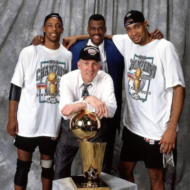 馬刺隊1998-99球季拿下隊史首座NBA總冠軍,總教練帕波維奇(前)與艾略特(後左)、羅賓森(後中)、鄧肯(後右)等人合影。(圖取自facebook.com/nba.taiwan)