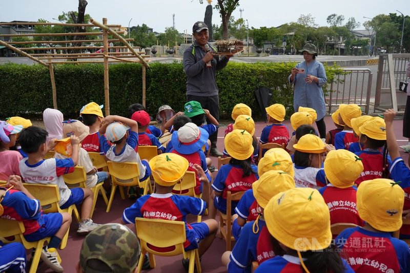 屏東縣來義鄉傳統狩獵文化協會2025年攜手來義鄉立幼兒園,9日在園內開課,帶領學童認識野生動物及生態環境,了解排灣族如何與山林共存。圖為協會文化講師江人頡(後中)向孩子們解說獵寮功能。中央社記者黃郁菁攝 114年5月9日