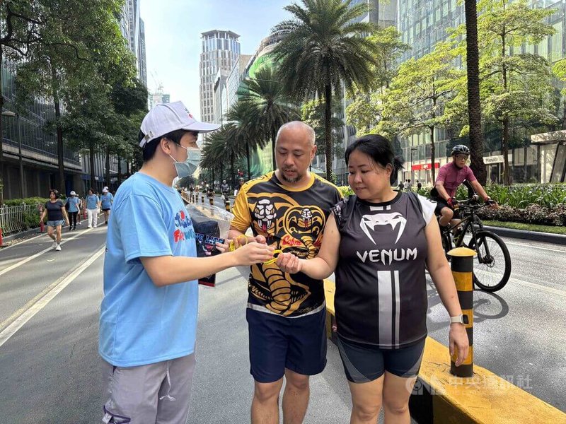 旅菲台商與僑界人士11日透過晨跑,支持台灣參與世界衛生組織(WHO)及世界衛生大會(WHA)。圖為一名台灣青年向菲國晨跑者發送宣傳手環。中央社記者林行健馬卡蒂市攝 114年5月11日