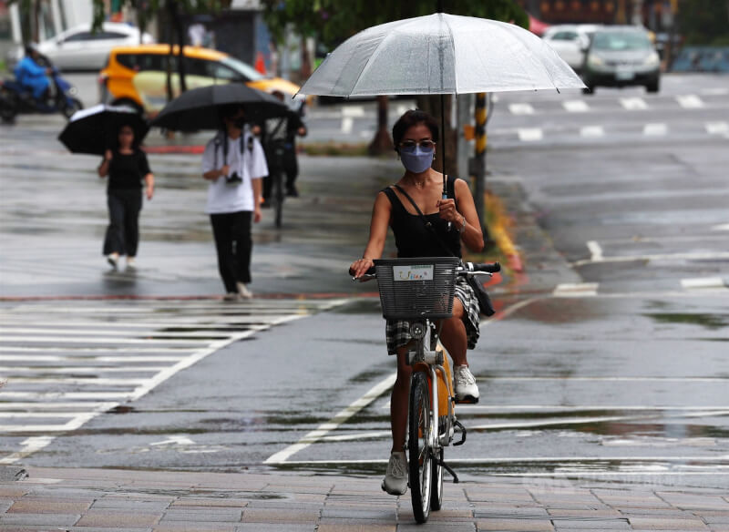 圖為台北市信義區民眾騎腳踏車撐傘遮擋雨勢。(中央社檔案照片)