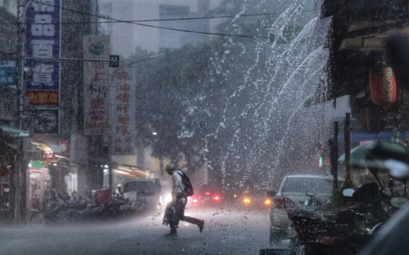 圖為台北市內湖區未帶傘具的民眾,頂著雨勢快步穿越馬路。(中央社檔案照片)