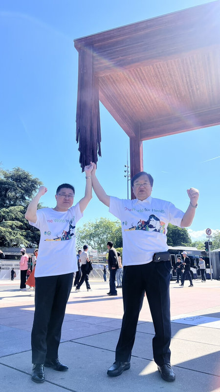 衛生福利部長邱泰源(右)與次長呂建德在世衛總部前廣場,象徵性撐起「三腳椅」塑像缺損的第4支腳,這個故事啟發貝里斯衛福部長柏納在世衛大會比喻「唯有納入台灣,這把椅子才能變得完整」。(衛福部提供)中央社記者田習如日內瓦傳真 114年5月22日