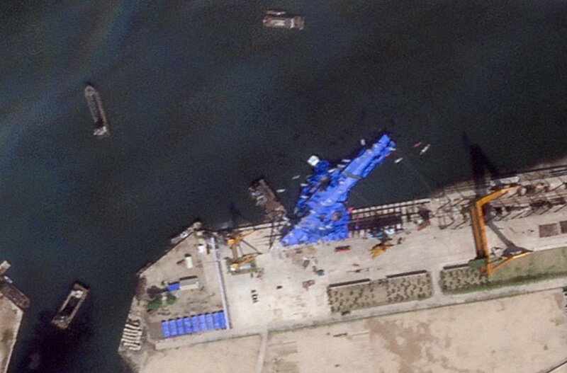 北韓21日在東部港口城市清津舉行的海軍新驅逐艦下水儀式發生事故。22日衛星影像顯示,軍艦上覆蓋藍色防水布,側翻在清津造船廠水中。(Planet Labs PBC/Handout via 路透社)
