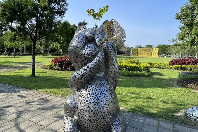 台南山上花園水道博物館入口廣場處的貓造型裝置藝術「幸福.召喚」,因作品中心鏤空,近日館方發現有一株植物從基座下方生長後,穿過作品從頭頂長出枝葉,有遊客覺得像動畫「龍貓」經典撐傘畫面。(館方提供)中央社記者楊思瑞台南傳真 114年5月25日