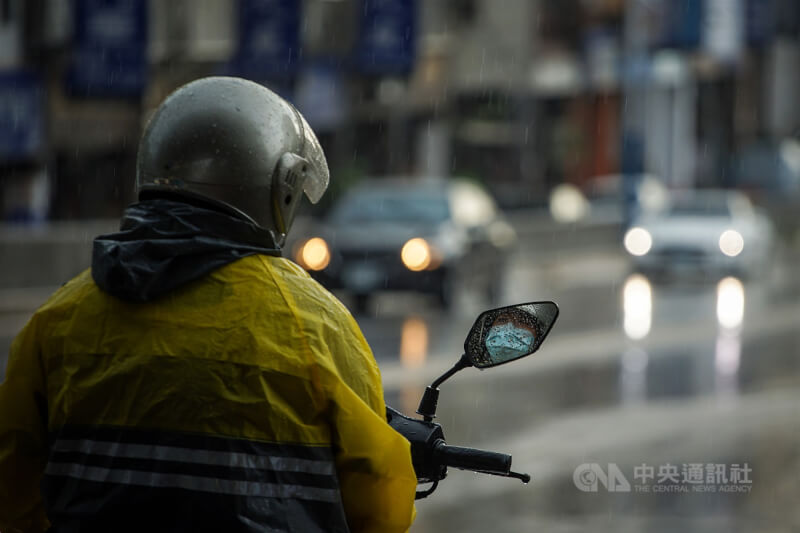 圖為台北市下起局部陣雨,機車騎士冒雨停等紅燈。(中央社檔案照片)