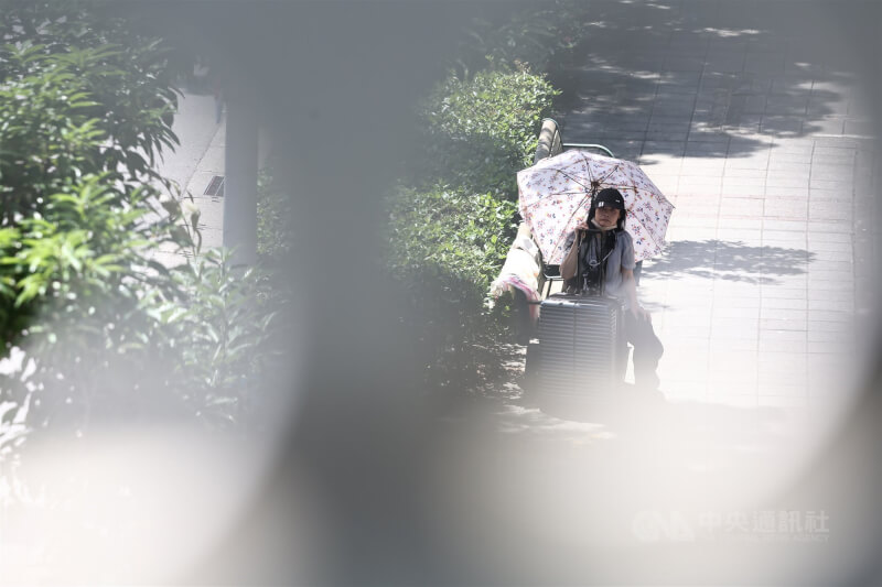 圖為台北市南港區民眾戴帽子、撐傘在陰涼處休息。(中央社檔案照片)