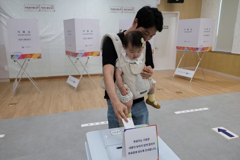 韓國3日舉行總統大選，一名選民背著嬰兒投票。（路透社）