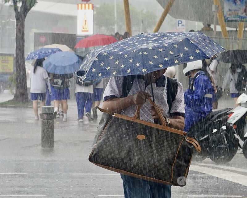 圖為高雄市民眾撐傘擋雨。(中央社檔案照片)