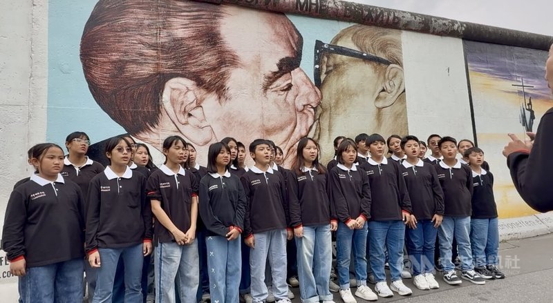 原聲童聲合唱團在德國柏林圍牆著名的「兄弟之吻」壁畫前演唱。快閃表演不僅吸引路人駐足,也讓來自台灣部落的孩子親身感受冷戰遺跡與世界歷史。中央社記者林尚縈柏林攝 114年6月10日