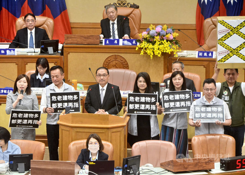 新北市長侯友宜(立者左3)13日列席市政總質詢,多名民進黨籍議員關切危老重建都更議題,直接站在侯友宜兩側舉牌表達立場訴求。中央社記者黃旭昇新北市攝 114年6月13日
