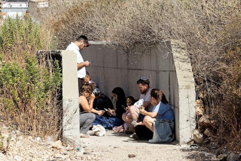 15日以色列中部地區響起飛彈警報,民眾躲在高速公路旁。(路透社)