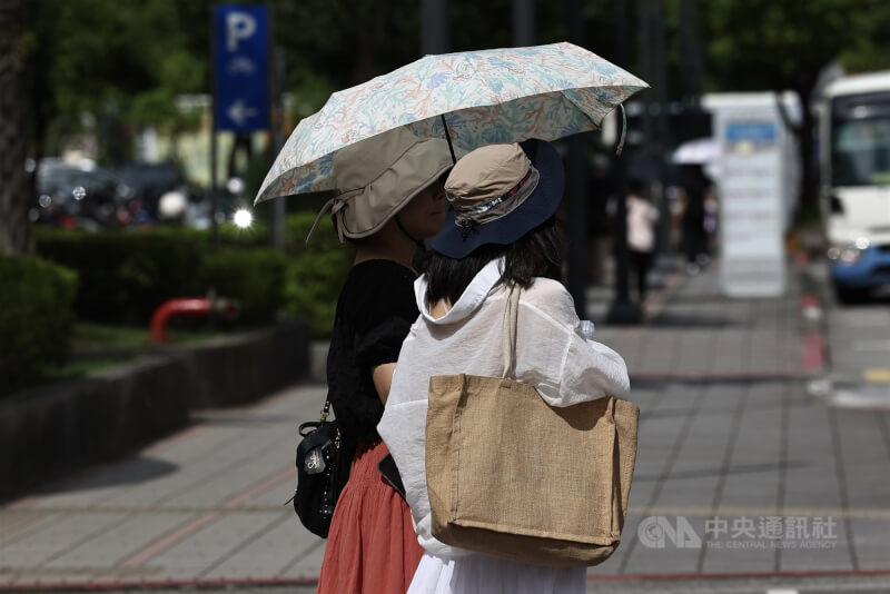 圖為台北市南港區民眾撐傘、戴遮陽帽等紅綠燈。(中央社檔案照片)