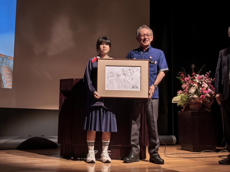 第31屆國際書法聯盟會員作品展6月20至23日在沖繩舉辦,特別安排主題設計比賽,獲得最優秀獎的那霸市立安岡中學學生林涵韵(左)受獎,並贈送作品給沖繩縣知事玉城鄧尼(右)。(張炳煌提供)中央社記者楊明珠東京傳真 114年6月27日