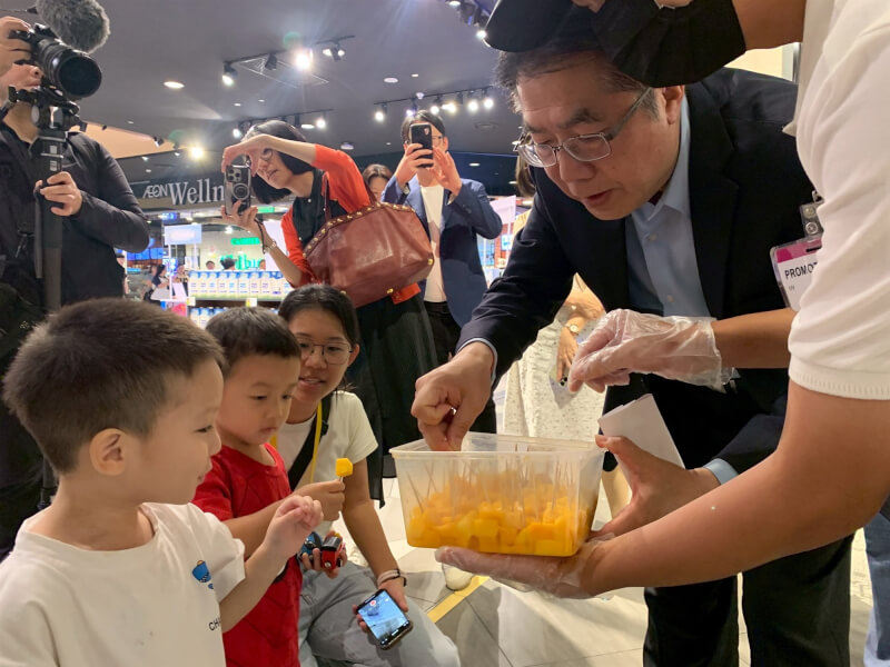 台南市長黃偉哲(右2)在吉隆坡當地大型連鎖超市向路過兒童分送試吃芒果。(台南市政府提供)