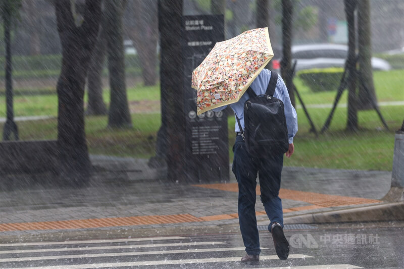 圖為新北市板橋區下起大雨,外出民眾撐傘前行。(中央社檔案照片)