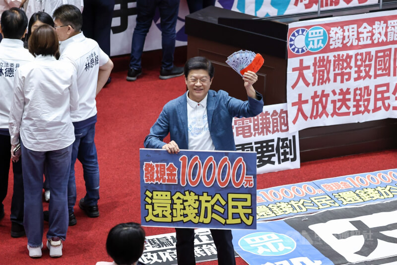 國民黨團11日召開黨團大會,決議處理新台幣4100億元特別條例草案,支持國土韌性的1500億元預算,並納入普發現金1萬元。圖為登記發言時,國民黨立委羅明才(中)拿著鈔票與標語留影。中央社記者翁睿坤攝 114年7月11日