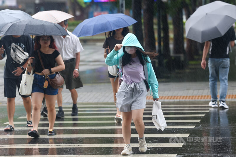 圖為新北市板橋區外出民眾拉起帽子、撐傘遮擋雨勢。(中央社檔案照片)