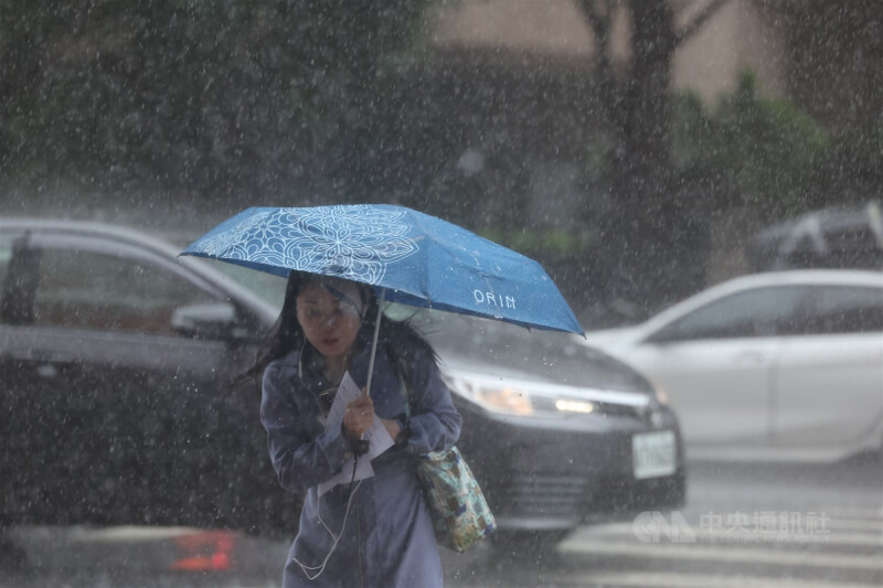 台北市中正區午後雷陣雨，民眾撐傘過馬路。（中央社檔案照片）