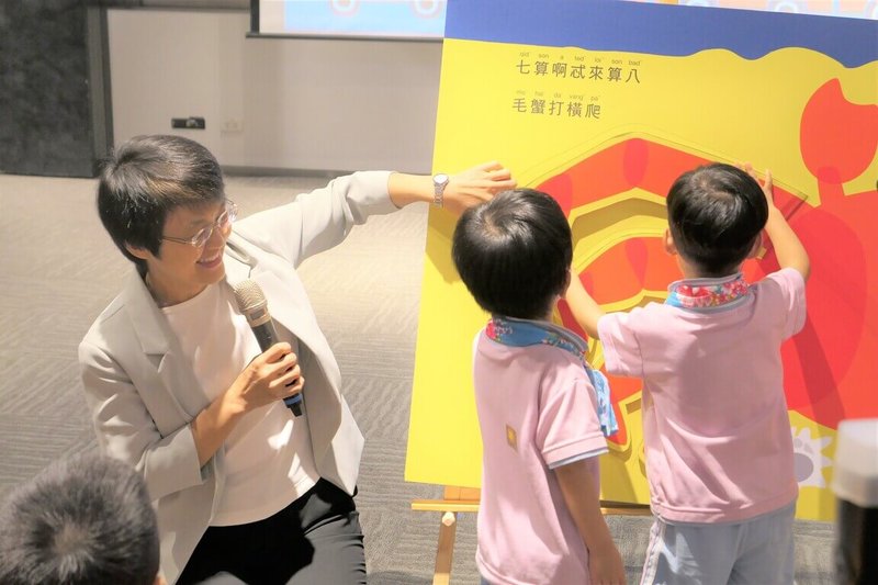 全台首套「嬰幼兒客語翻翻書」23日亮相,客委會主委古秀妃(左)與樟新幼兒園小朋友共讀巨型翻翻書,用客語細數毛蟹有幾隻腳,讓講客語變得更生動有趣。(客委會提供)中央社記者汪淑芬傳真 114年7月23日