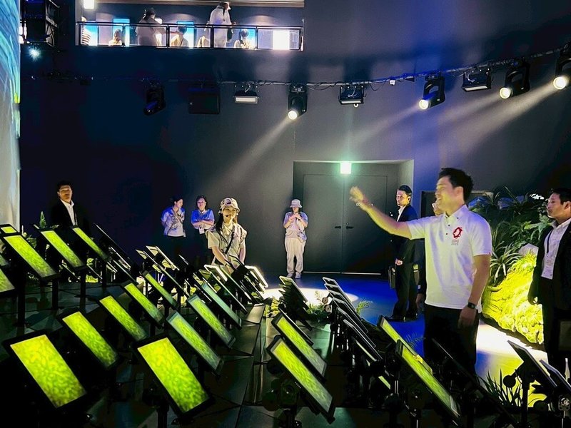 大阪府知事吉村洋文(右2)26日造訪大阪世博TECH WORLD館,觀賞多個顯示器同步顯示畫面,形成一片「花海」,揮動手臂與顯示器互動。(TECH WORLD館提供)中央社記者戴雅真東京傳真 114年7月27日